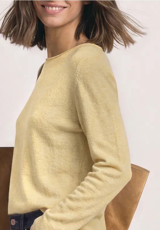 Seitliche Ansicht einer Frau in hellgelbem Pullover, entspannt lächelnd im lässigen Casual-Look.