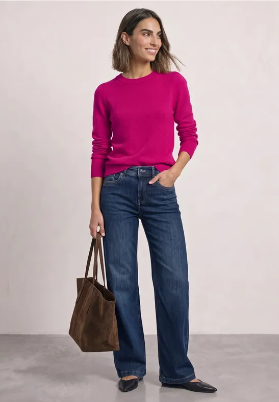 Femme en pull fuchsia et jean large, portant un sac marron.