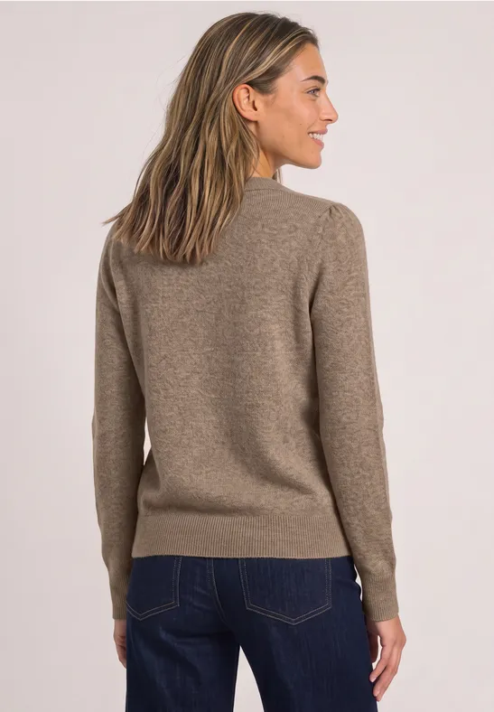 Frau von hinten in braunem Pullover und Jeans vor hellem Hintergrund.