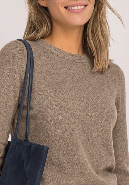 Frau im braunen Pullover mit dunkelblauer Schultertasche und leichtem Lächeln.