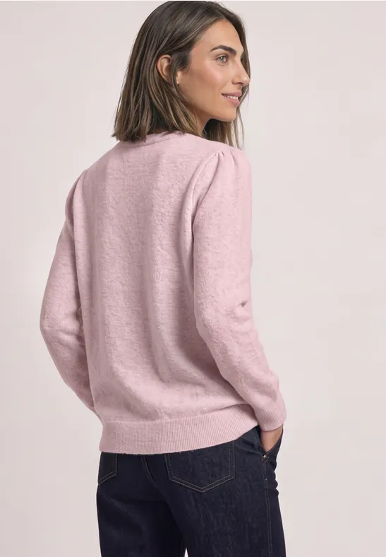 Eine Frau trägt einen rosa Pullover und dunkle Jeans, Blick seitlich und von hinten.