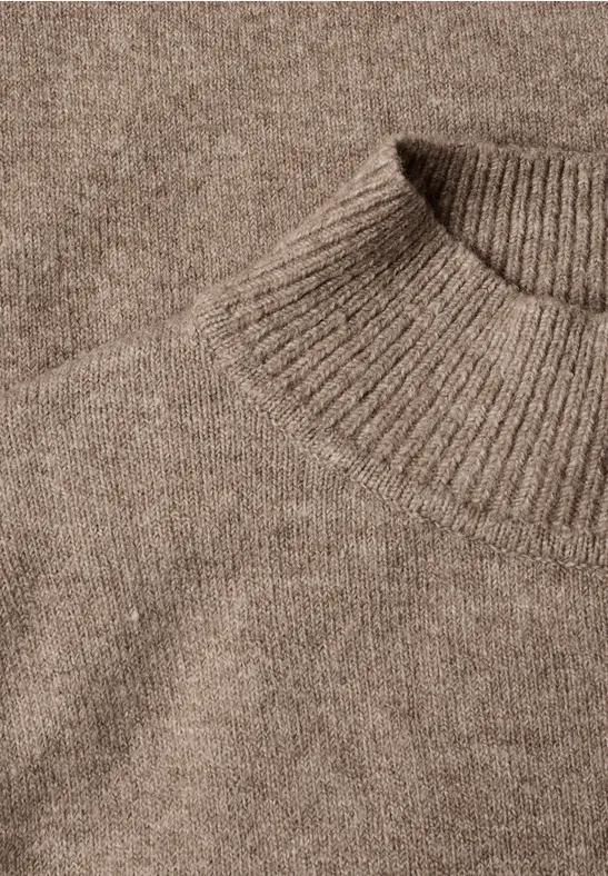 Gros plan d’un pull en laine beige tricotée, mettant en avant l’encolure ronde.