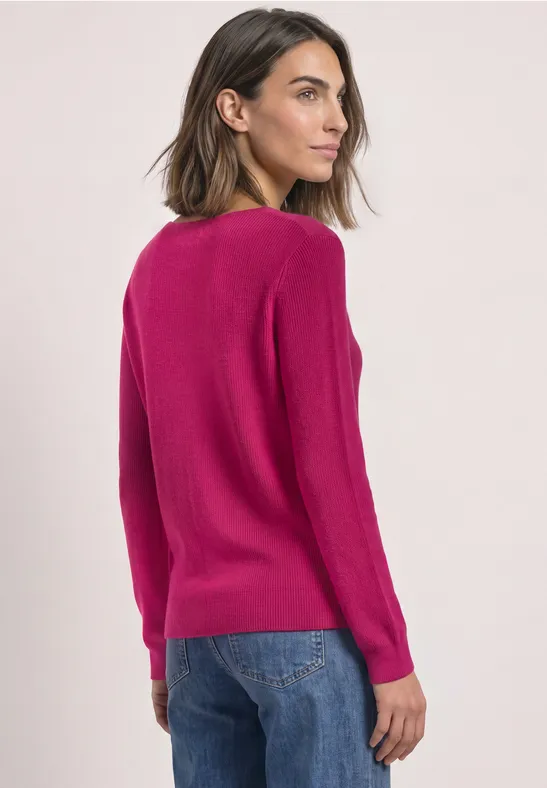 Frau von hinten in pinkem Pullover und Jeans vor hellem Hintergrund.
