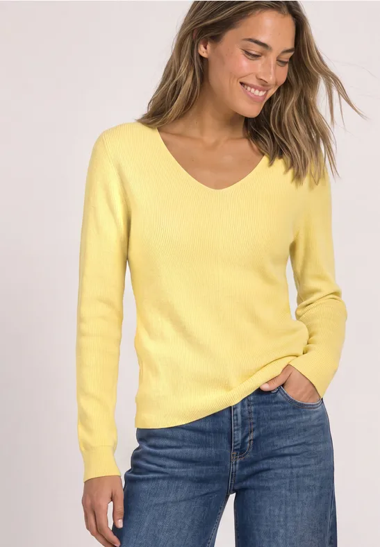 Lächelnde Frau im gelben V-Pullover und blauen Jeans.