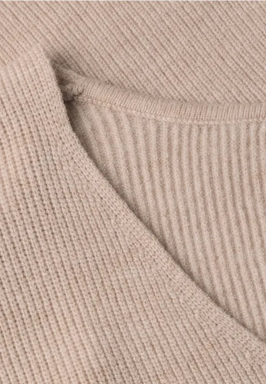 Gros plan d’un pull en maille beige côtelée avec col en V.