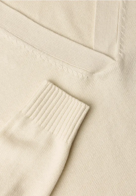 Nahe Aufnahme eines cremefarbenen Strickpullovers mit V-Ausschnitt und Rippbündchen.