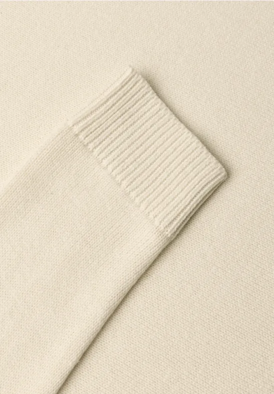 Nahaufnahme eines cremefarbenen Strickpullover-Ärmels mit Rippbündchen