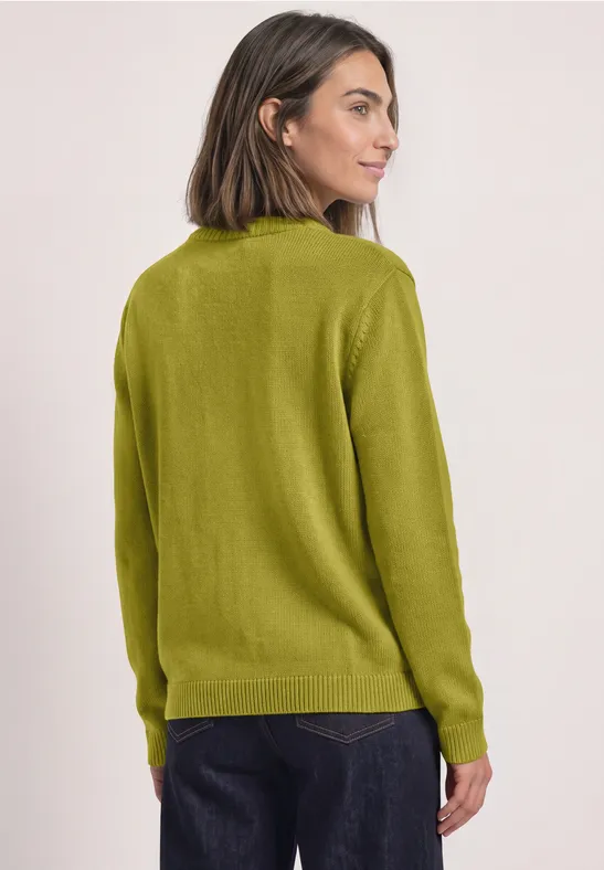 Frau in grünem Pullover, leicht zur Seite gedreht, Blick über die Schulter.