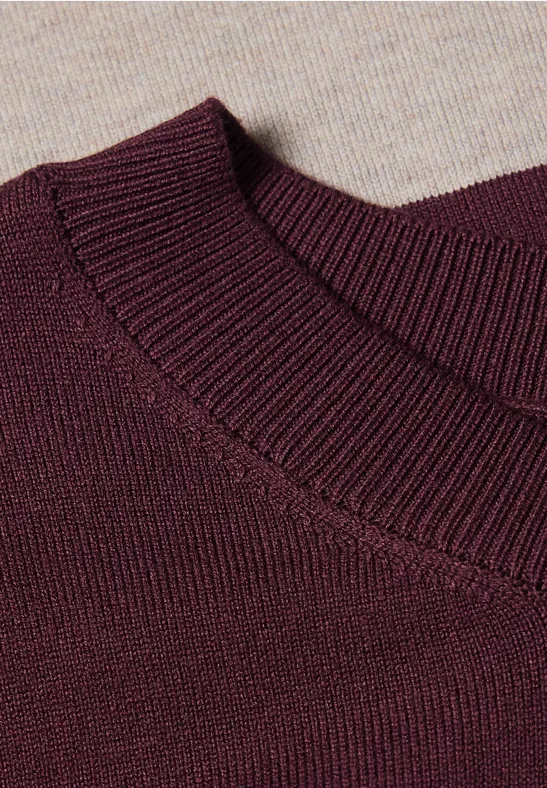 Nahaufnahme eines burgunderroten Strickpullover-Ausschnitts auf beigem Strickuntergrund.