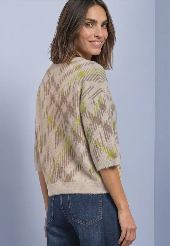 Frau in beigem Strickpullover mit Karomuster, schaut über die Schulter.