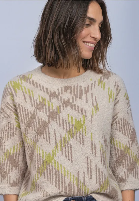 Eine lächelnde Frau mit schulterlangem Haar trägt einen beigen Pullover mit grünem Karomuster.