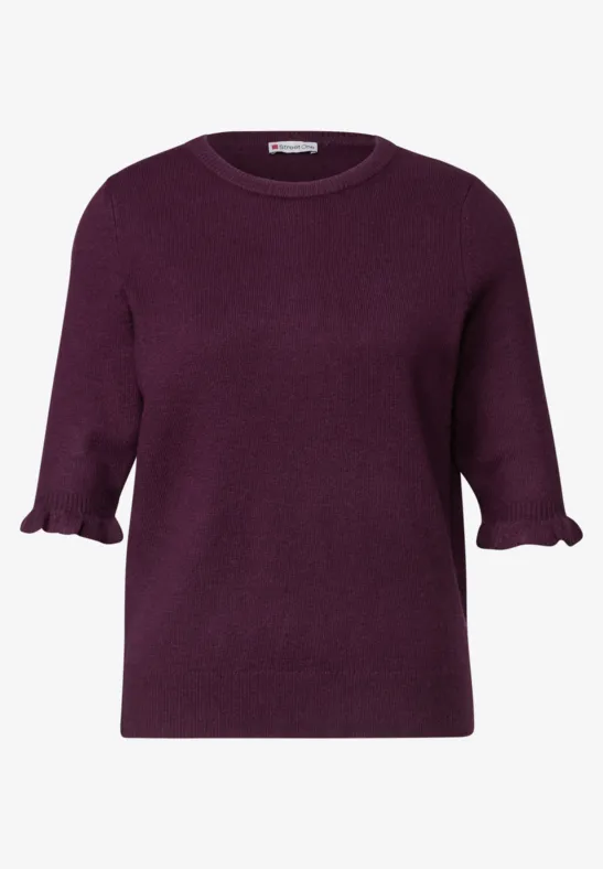 Ein schlichtes, dunkellila Strickshirt mit 3/4-Ärmeln und Rüschen an den Ärmelenden.