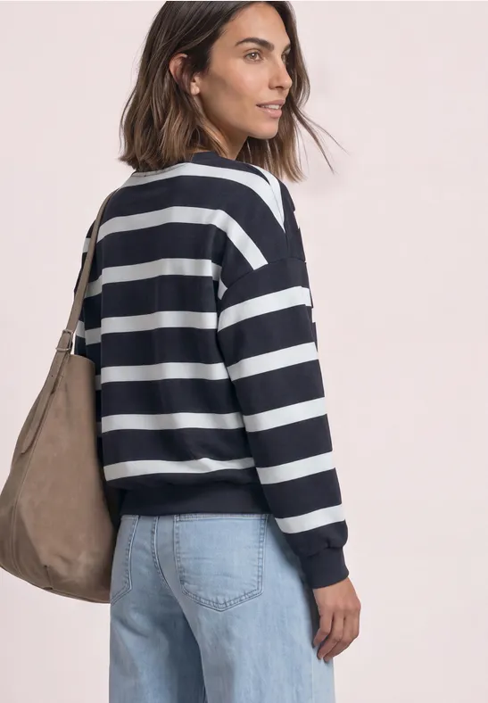 Een vrouw in een marine-wit gestreepte trui en lichte jeans met een schoudertas, zijaanzicht.