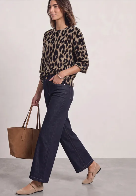 Moderne Frau in Leopardenpullover, weitem Jeans, beigen Absätzen und großer brauner Tasche.
