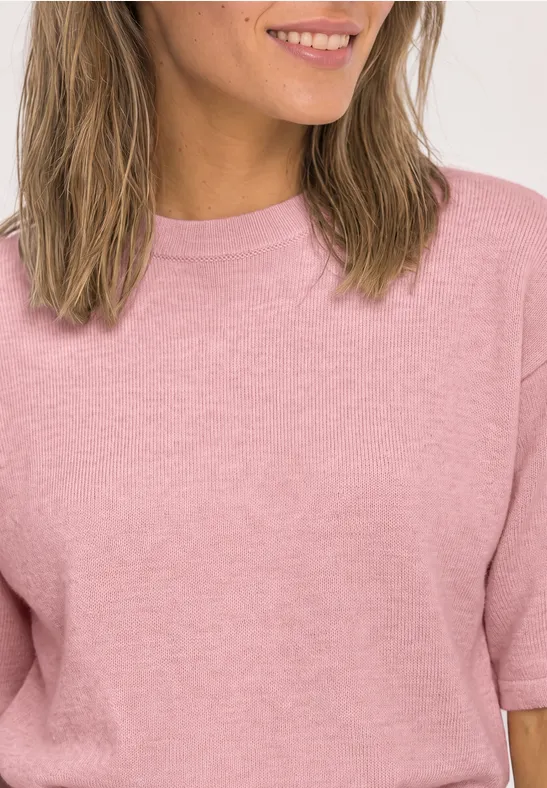 Frau in rosa T-Shirt mit schulterlangen Haaren, lächelt sanft.