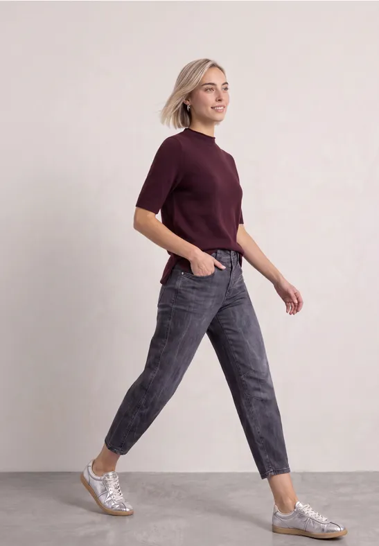 Eine junge Frau in bordeauxfarbenem T-Shirt und grauen Jeans läuft dynamisch, trägt silberne Sneaker.