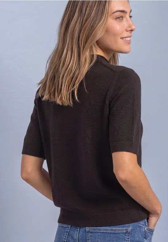 Frau von hinten in schwarzem Kurzarm-Pullover und Jeans, im Profil lächelnd.