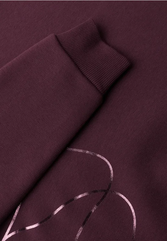 Nahaufnahme eines weinroten Sweatshirts mit glänzendem Linien-Print auf dem Ärmel.