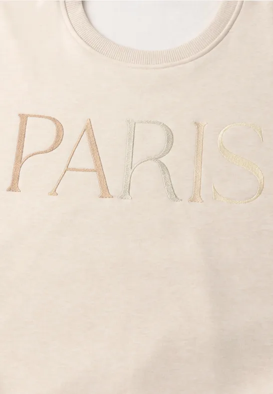 Beiges T-Shirt mit dem Schriftzug PARIS in großen, eleganten Buchstaben.