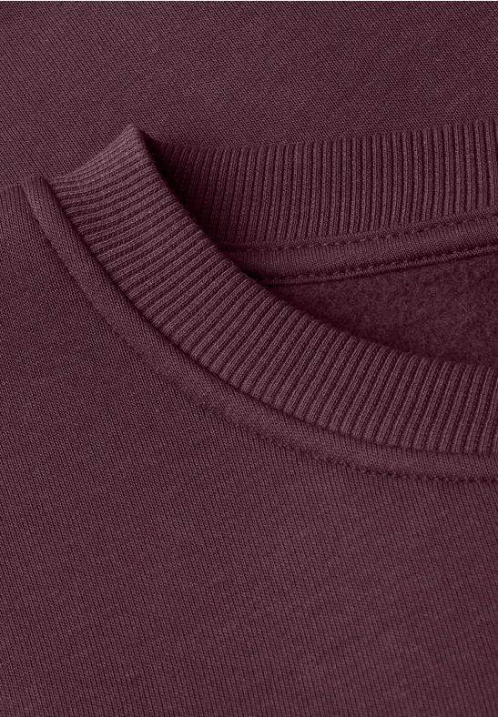 Close-up van een bordeauxrood sweatshirt met ronde hals en geribde boord.