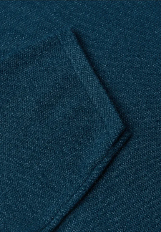 Nahaufnahme eines dunkeltürkisen Strickstoffes mit einer aufgesetzten Tasche.