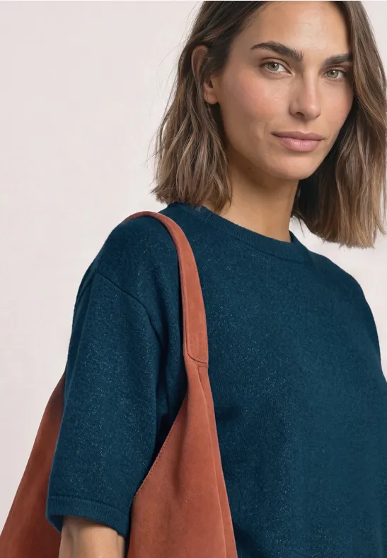 Frau mit schulterlangem Haar in dunkelblauem Kurzarm-Pullover, trägt eine braune Ledertasche.