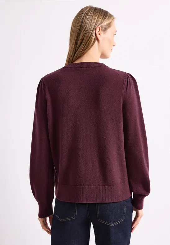 Femme de dos portant un pull violet foncé à manches bouffantes et un jean.