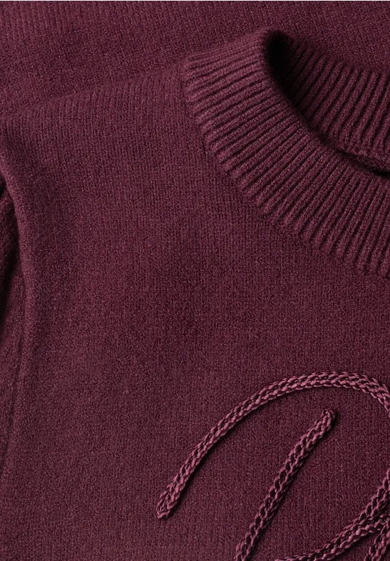 Gros plan d’un pull en maille bordeaux à col rond avec texture fine.