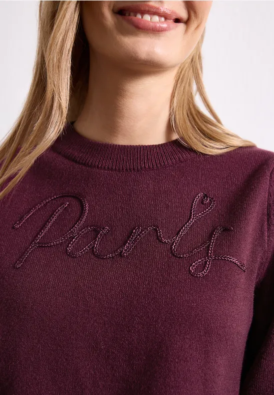Femme en pull bordeaux avec l'inscription brodée 'Paris'.