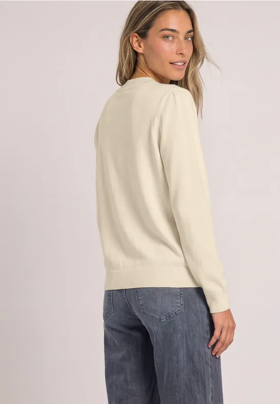 Frau in hellem Pullover und Jeans blickt lächelnd über die Schulter.