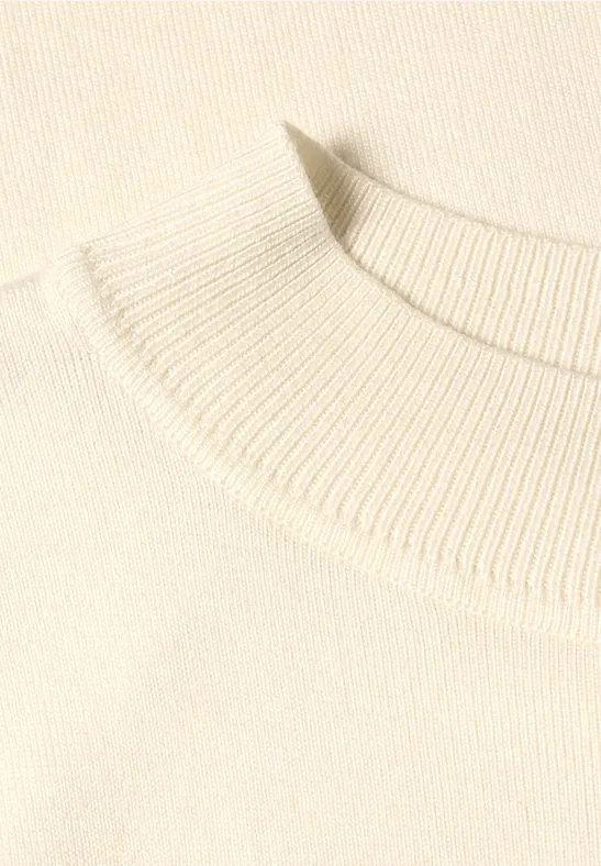Nahaufnahme des schlichten, cremefarbenen Strickkragens eines Pullovers.