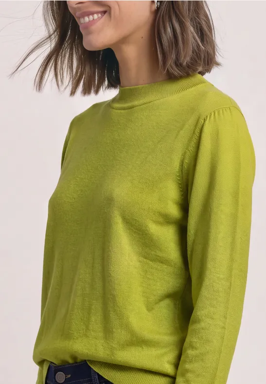 Eine lächelnde Frau mit schulterlangem Haar trägt einen limonengrünen Pullover und blickt zur Seite.
