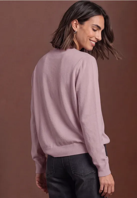 Frau in rosa Pullover und dunkler Jeans von hinten, dreht den Kopf und lächelt.