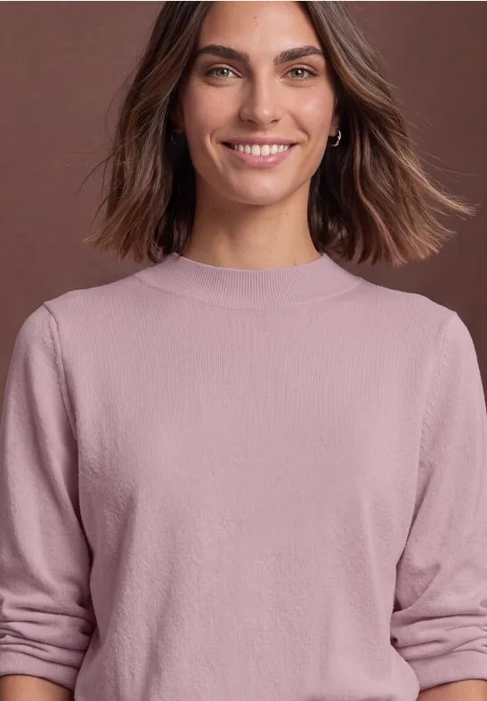 Lächelnde Frau mit braunen Haaren und rosa Pullover vor neutralem Hintergrund.