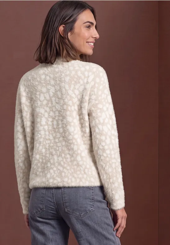 Frau im Profil von hinten in cremefarbenem, flauschigem Pullover mit dezentem Muster und blauen Jeans.