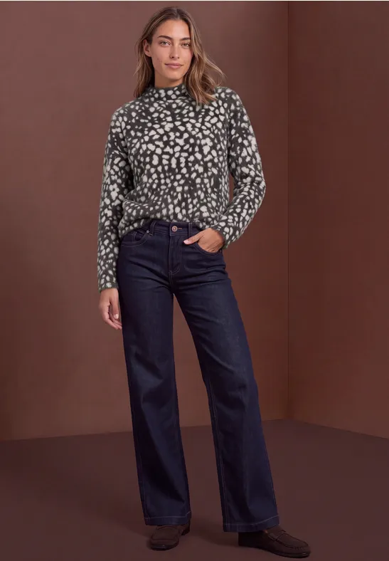 Frau in Rollkragenpullover mit Leopardenmuster und dunkler weiter Jeans vor braunem Hintergrund.