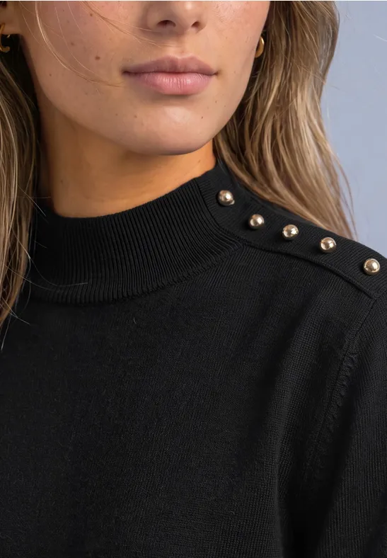 Nahaufnahme einer Frau im schwarzen Pullover mit goldenen Nieten auf der Schulter.