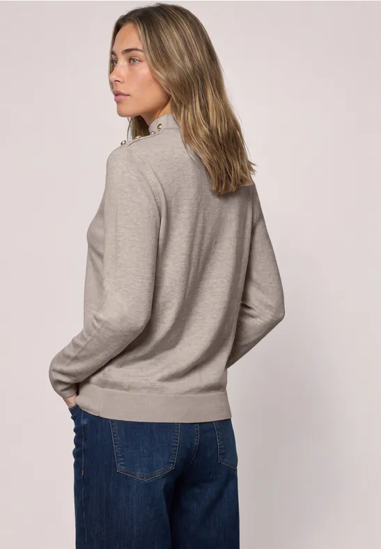 Frau von hinten in hellgrauem Pullover und blauer Jeans, schaut seitlich, neutraler Hintergrund.