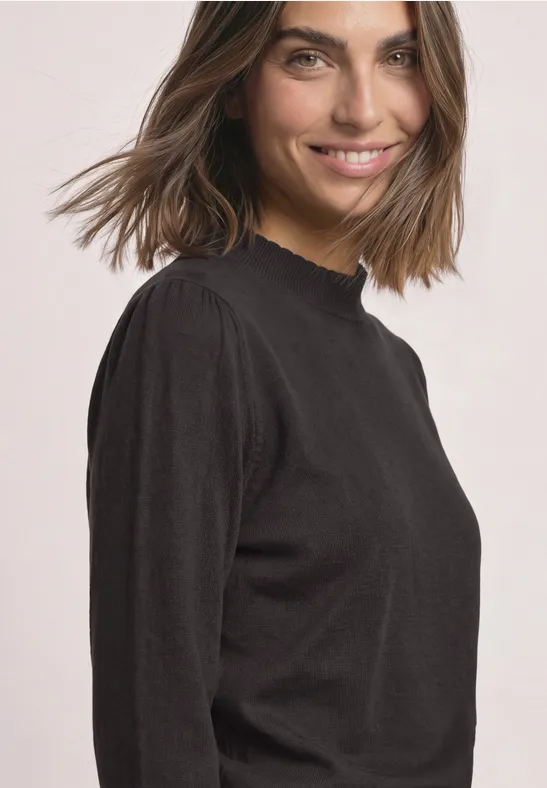 Lächelnde Frau in schwarzem Langarmshirt vor hellem Hintergrund.
