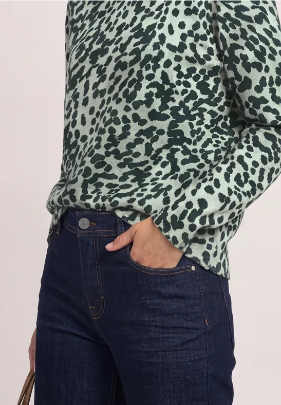Vrouw in groen gevlekt overhemd en donkerblauwe jeans met een hand in de zak.