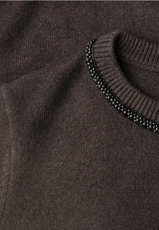 Nahaufnahme eines dunkelbraunen Strickpullovers mit schwarzer Perlenverzierung am Rundhalsausschnitt.