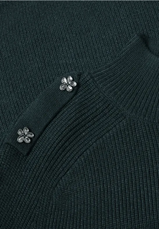 Nahaufnahme eines dunkelgrünen Strickoberteils mit zwei silbernen Blumenknöpfen