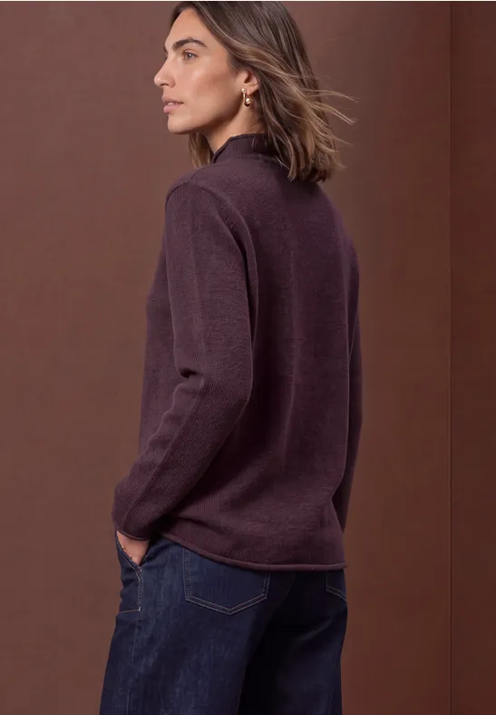 Seitenansicht einer Frau in violettem Pullover und Jeans vor braunem Hintergrund.