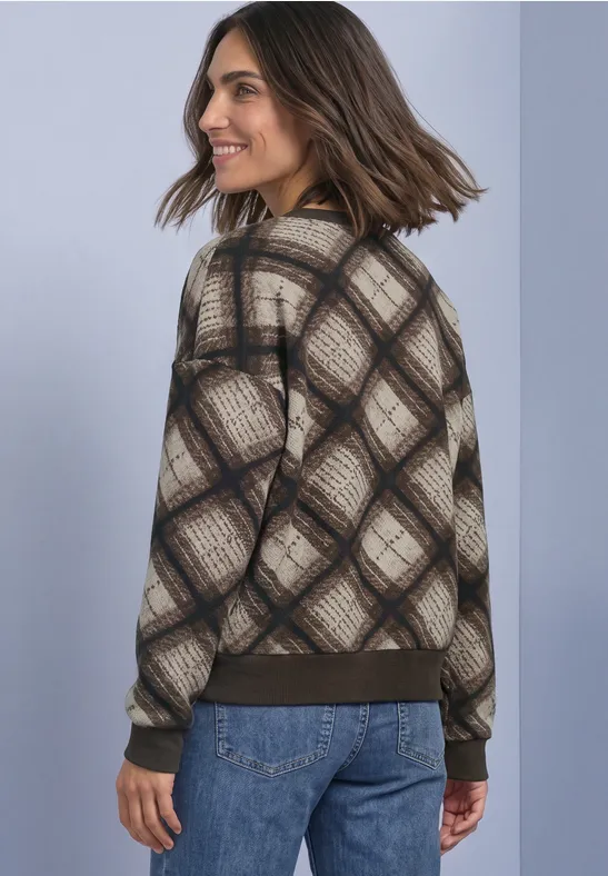 Femme souriante en pull à carreaux et jeans, regardant de côté.