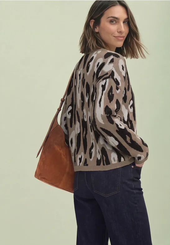 Frau mit Leopardenmuster-Pullover, dunklen Jeans und brauner Wildledertasche, schaut über die Schulter.