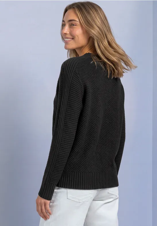 Frau in schwarzem Pullover und heller Hose blickt lächelnd über die Schulter.