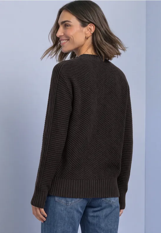 Frau in schwarzem Strickpullover und blauen Jeans von hinten, mit schulterlangem Haar, lächelnd.