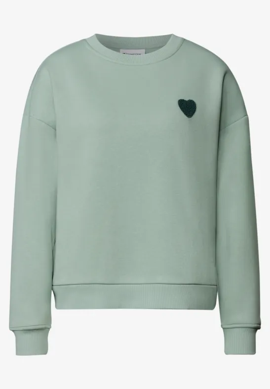 Ein mintgrüner Pullover mit kleinem schwarzen Herz auf der Brust.