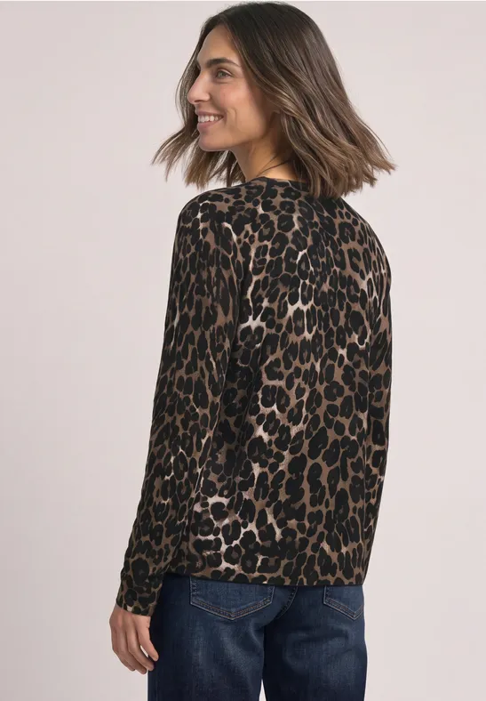 Eine Frau trägt einen braunen Leoparden-Pullover und blaue Jeans, schaut über die Schulter und lächelt.