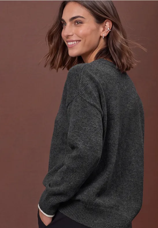 Frau mit kurzen braunen Haaren in grauem Strickpullover, lächelnd und über die Schulter blickend